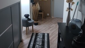 Moderni olohuone, jossa on kalteva katto, puulattia, harmaa sohva, musta sohvapöytä, maljakko kukkineen ja taulu seinällä.