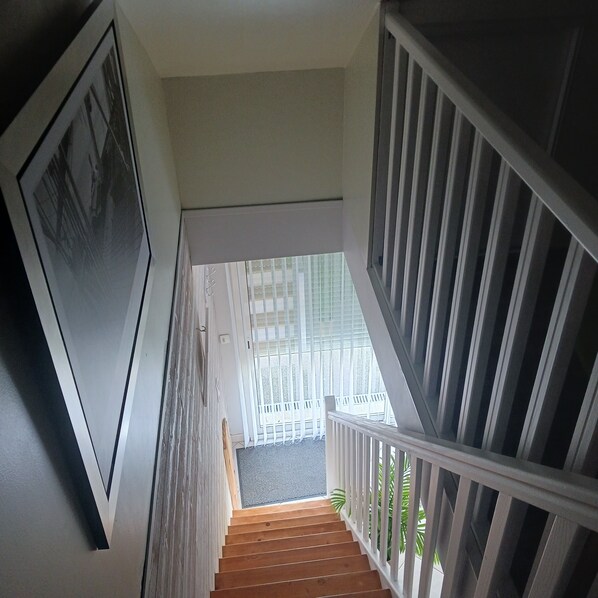 A staircase with wooden steps and white railings leading to a balcony with a view of a building.