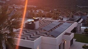 A modern building with a rooftop terrace, solar panels, and a view of the sunset over the ocean.