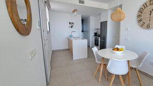 A modern kitchen with a central island, a dining area with a white table and chairs, and a large wall clock.