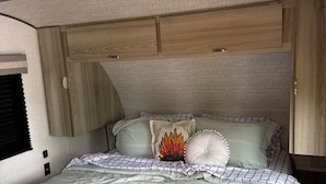 Een slaapkamer met een bed, kussens, een deken en ingebouwde houten kasten.