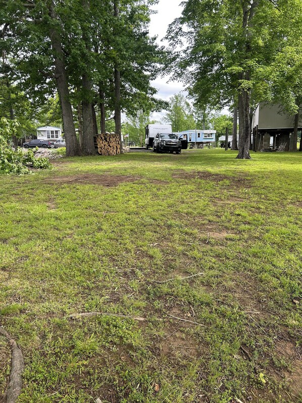 A grassy area with trees, a trailer, and a building in the background. - Tennessee River RV Retreat (Lobelville)