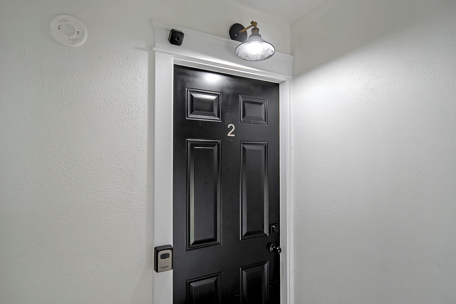 A black door with the number 2, a light fixture above it, and a wall-mounted intercom.