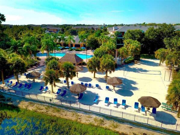 Ein Resort mit Schwimmbad, Liegestühlen, Palmen und einem eingezäunten Strandbereich.