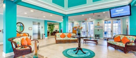 Een ruime lobby met turquoise wanden, rieten meubels en een centrale tafel.