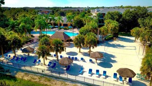 Een resort met een zwembad, ligbedden, palmbomen en een omheind strand.