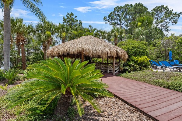 A thatched-roof structure with outdoor seating and a pathway leading to it.