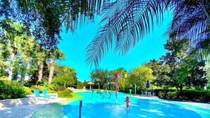 Een waterpark met een blauw zwembad, speeltoestellen en ligbedden.