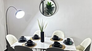 A dining area with a white table set for four, black tableware, and a potted plant. - Modern 3BR Hideaway in Masaki | Pool, Gym & Prime Location (Dar es Salaam)