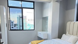 A modern bedroom with a large bed, a window with a city view, and a white wardrobe. - Modern 3BR Hideaway in Masaki | Pool, Gym & Prime Location (Dar es Salaam)