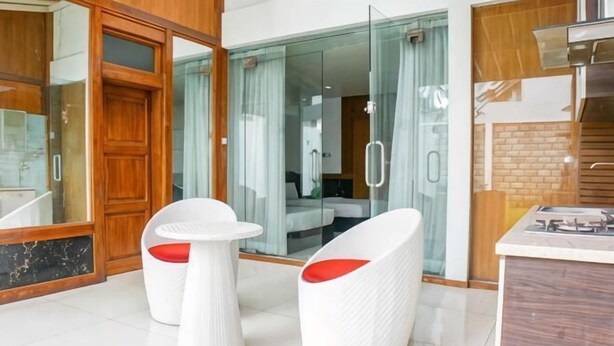 A modern hotel room with a glass door leading to a balcony, a kitchen area, and two white chairs with red cushions. - Hi Quality Dago by My Hospitality (Coblong)
