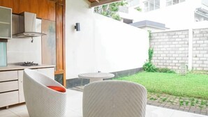 A modern kitchen with white cabinets, a built-in stove, and a dining area with a round table and two chairs. - Hi Quality Dago by My Hospitality (Coblong)