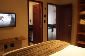 A hotel room with a bed, a TV mounted on the wall, a wooden door, and a shelf with a remote control. - Lume Beach House  (São Miguel do Gostoso)