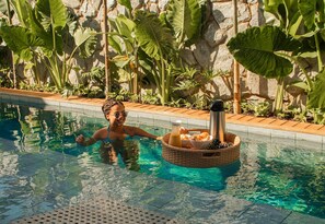 A pool with clear water, surrounded by tropical plants and a stone wall. - Lume Beach House  (São Miguel do Gostoso)