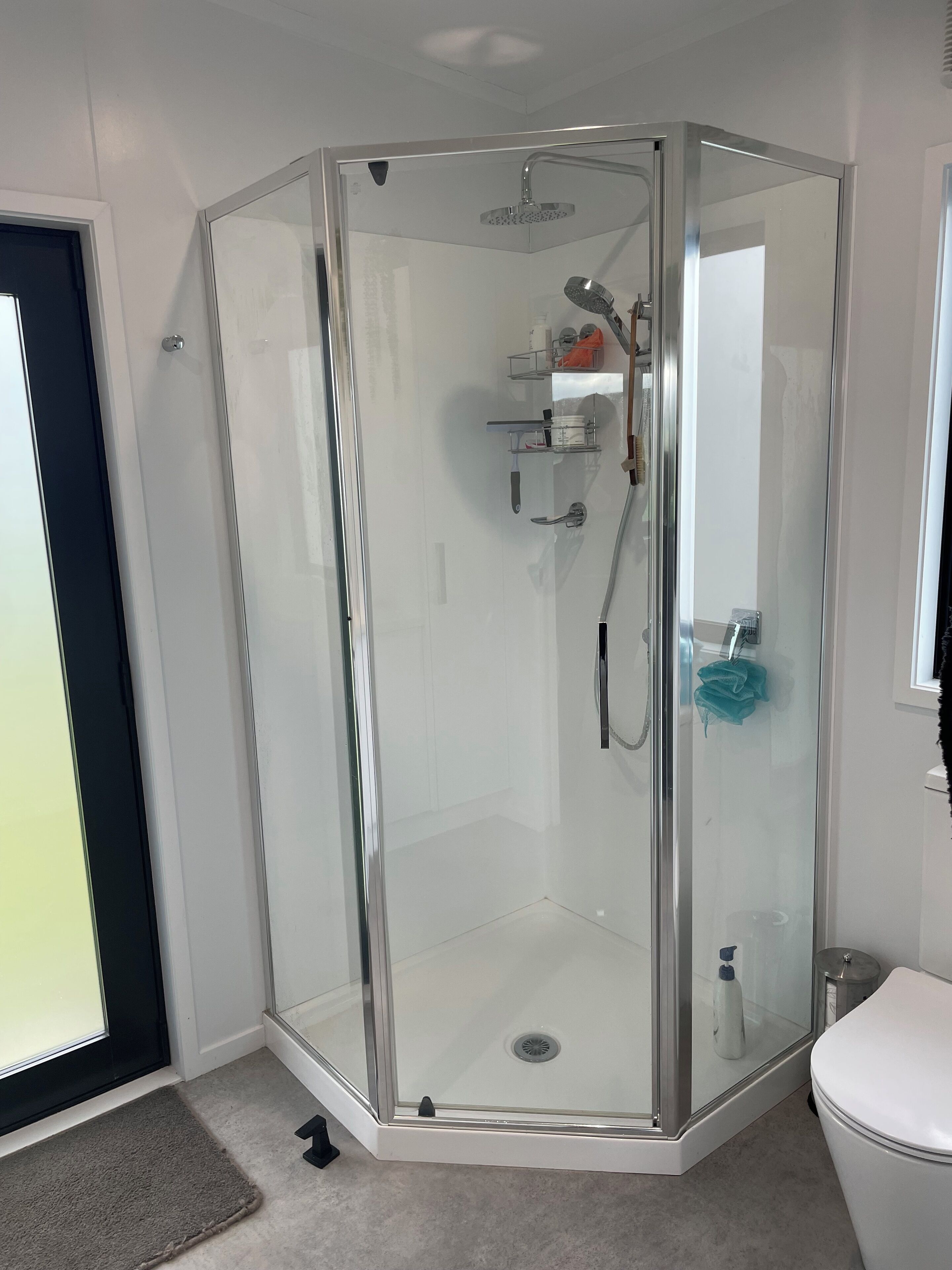 A corner shower with a glass enclosure, a toilet, and a small shelf with toiletries.