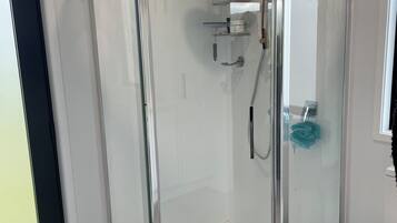 A corner shower with a glass enclosure, a toilet, and a small shelf with toiletries.