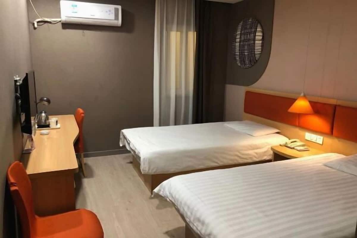 Ein Hotelzimmer mit zwei Einzelbetten, einem Schreibtisch mit Stuhl, einem Telefon und einer Wand-Klimaanlage.
