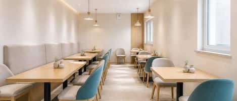A modern dining area with long tables and chairs, a window, and pendant lighting.