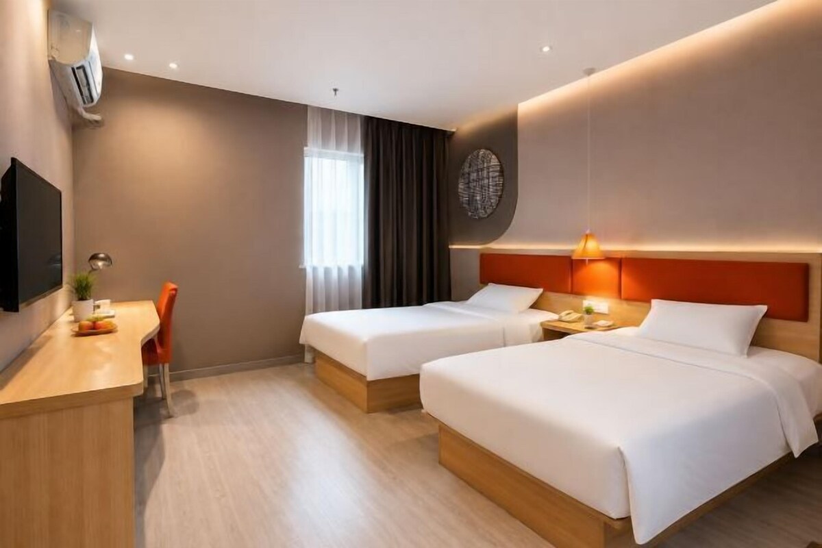 Habitación de hotel con dos camas, un escritorio, una silla, televisión y ventana con cortinas.