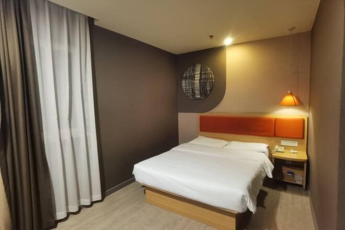 Ein Hotelzimmer mit Bett, Nachttisch, Lampe und Vorhängen.