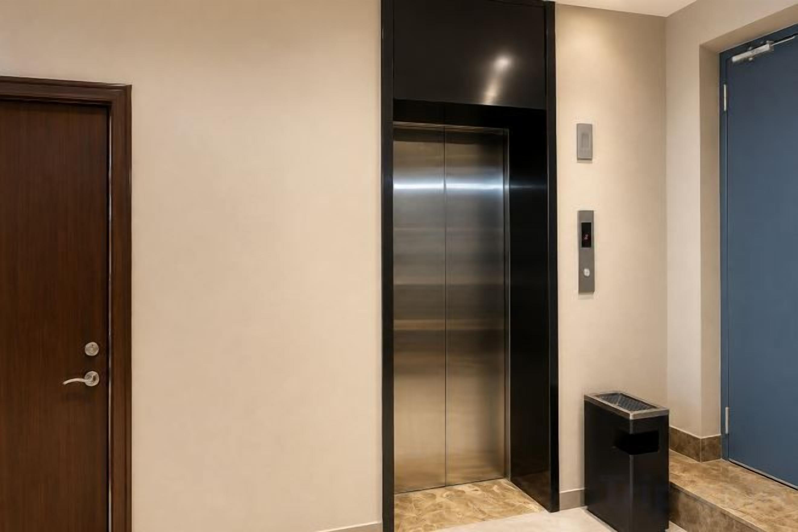 An elevator with a metallic finish, a door with a handle, and a trash bin beside it.