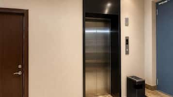 An elevator with a metallic finish, a door with a handle, and a trash bin beside it.