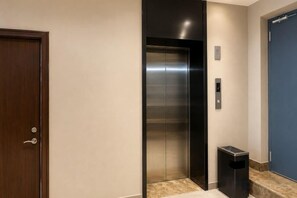 An elevator with a metallic finish, a door with a handle, and a trash bin beside it. - Yijia Hotel (Xinyi Railway Station Nanjing Road) (Xinyi)