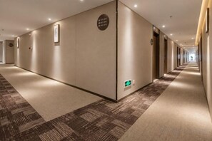 Pasillo de hotel con piso alfombrado, puertas a la derecha y un letrero de salida de emergencia verde.