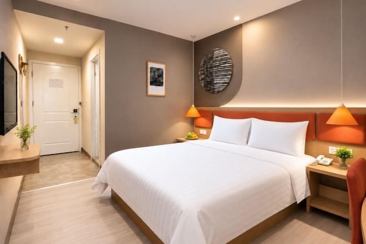 A hotel room with a large bed, bedside lamps, a flat-screen TV, and a door leading to another room.