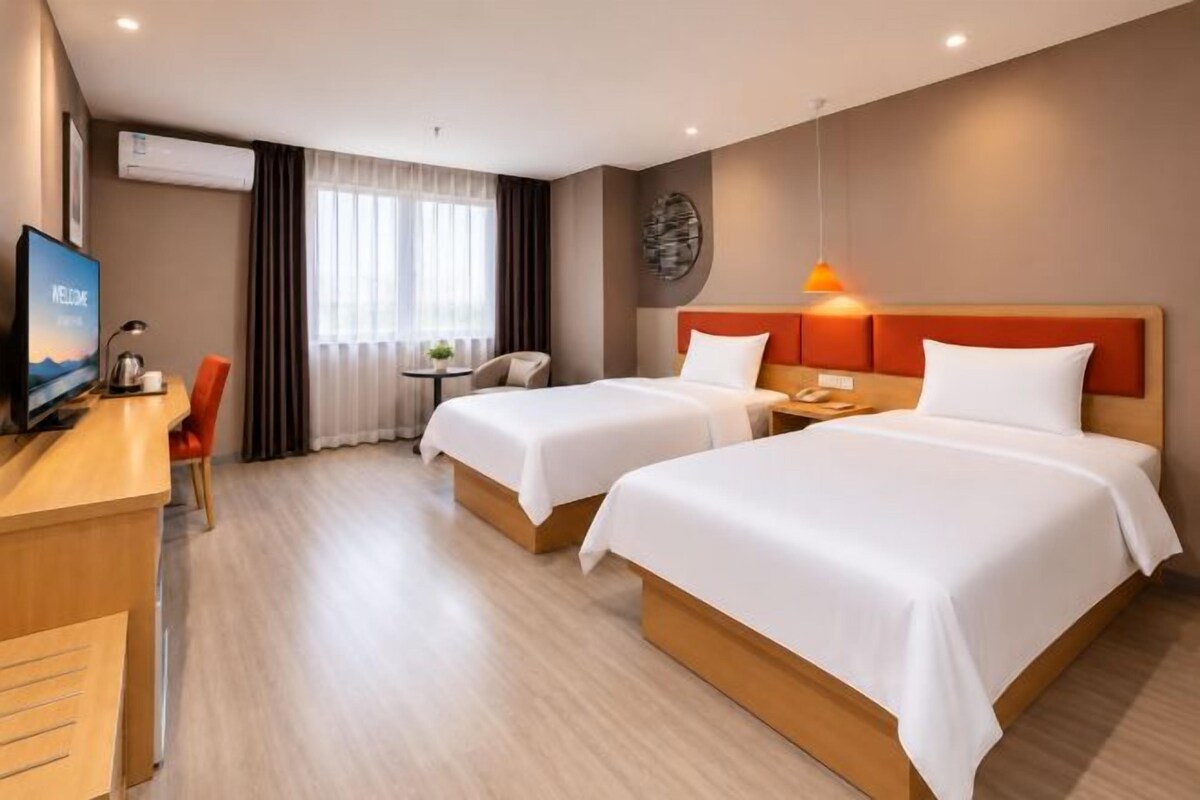 A hotel room with two beds, a desk, a TV, and a window with curtains.