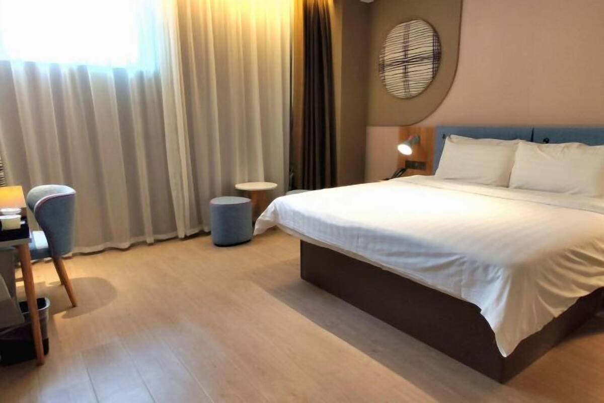 Ein Hotelzimmer mit Bett, Schreibtisch, Stuhl, Lampe und einem Fenster mit Vorhängen.