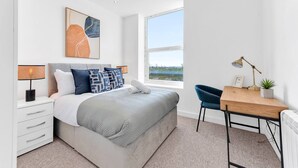 A bedroom with a bed, bedside tables, a desk, and a window with a view.