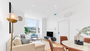 A modern living room with a sofa, chairs, a coffee table, a TV, and a dining table.