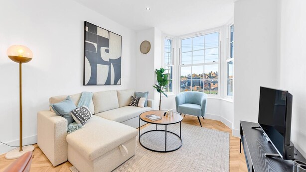 A modern living room with a sofa, a coffee table, a TV, and a large window offering a city view.