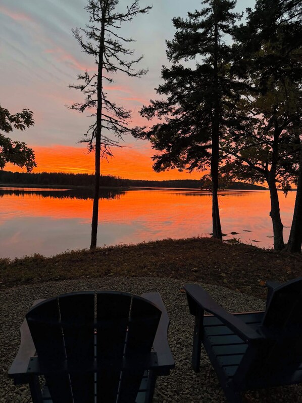 A lakeside view with two Adirondack chairs facing the sunset.