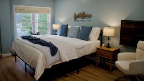 A bedroom with a large bed, two bedside lamps, a nightstand, a chair, and a wall-mounted artwork.