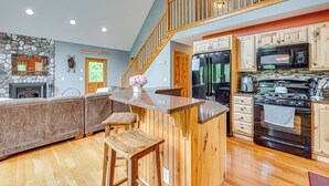 Una cocina amplia con chimenea de piedra, barra de madera y una escalera que lleva a un nivel superior.