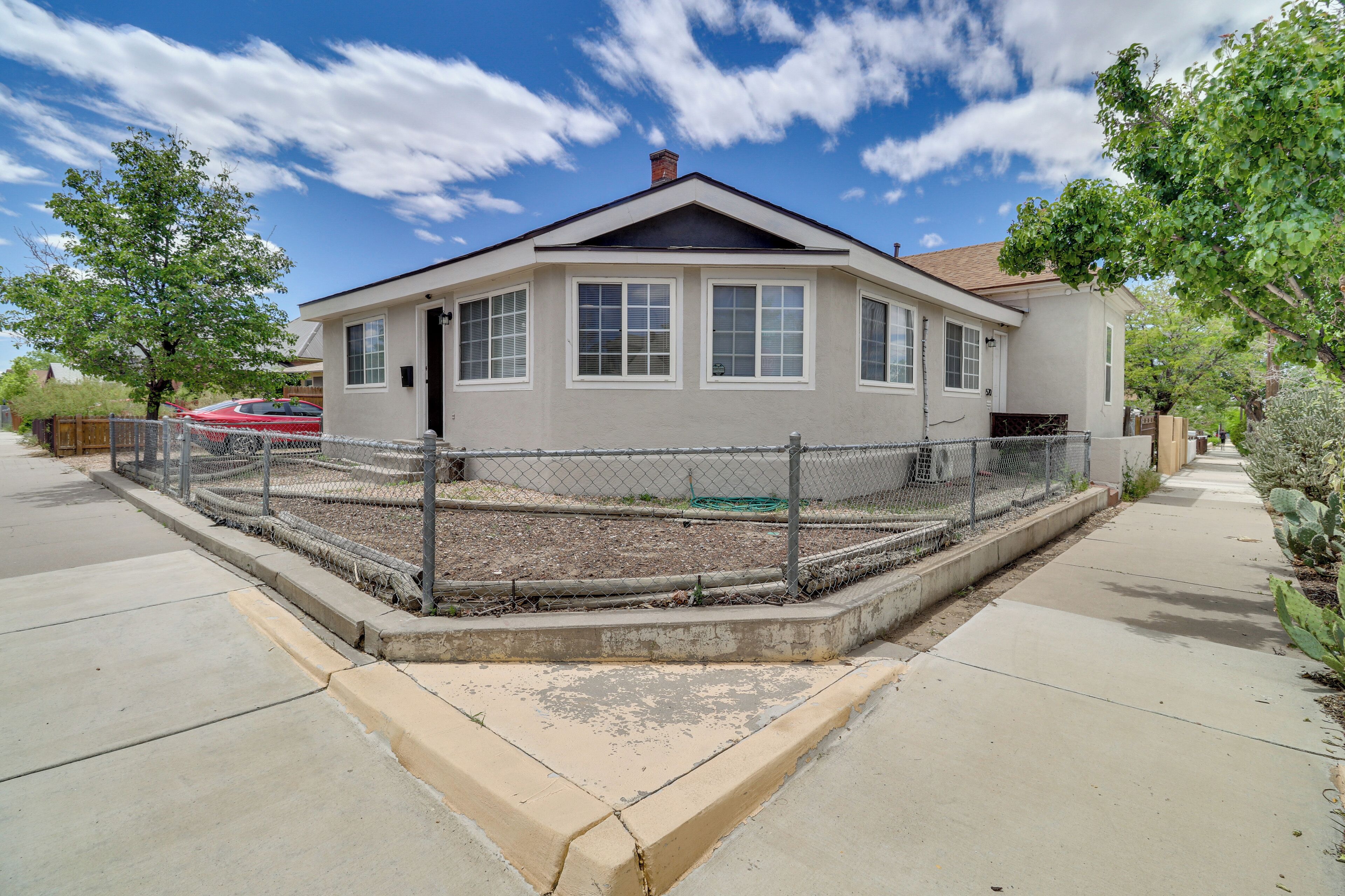 A single-story house with a fenced yard, a paved driveway, and a clear blue sky.