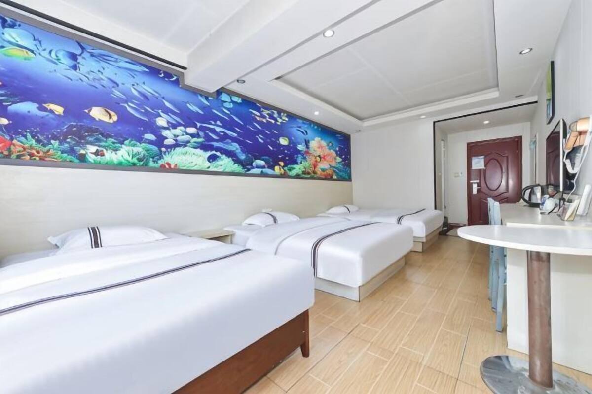 A hotel room with two beds, a large wall mural, a round table, and a door.