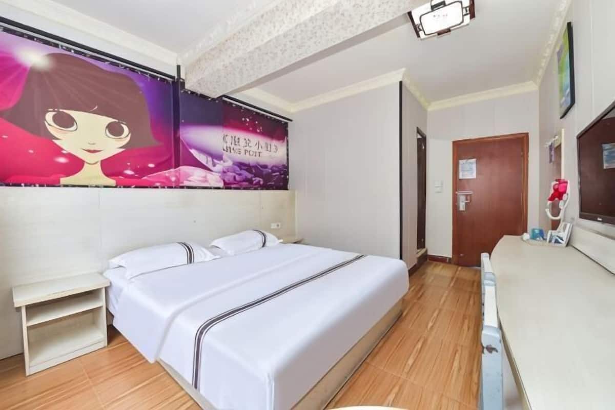 A hotel room with a bed, a small bedside table, a desk with a chair, and a wall-mounted TV.
