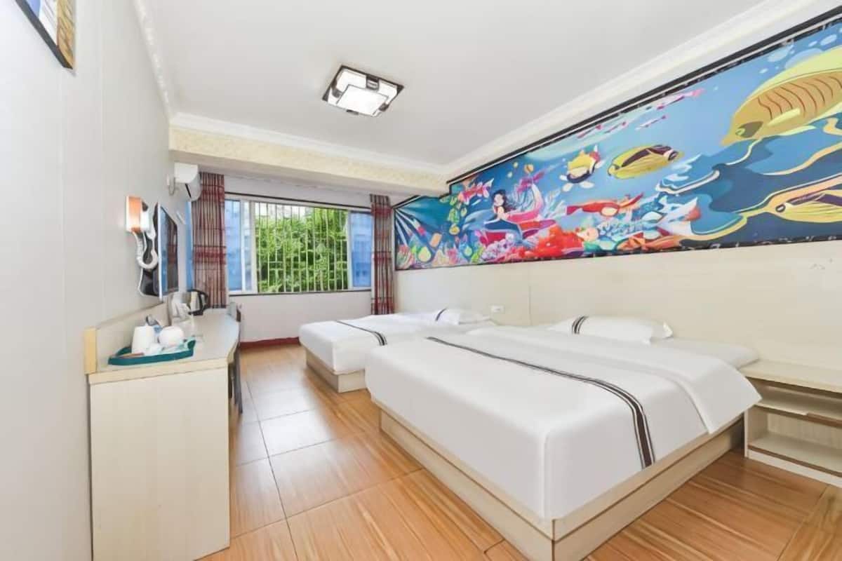 A hotel room with two beds, a small desk, a window with curtains, and a colorful mural on the wall.