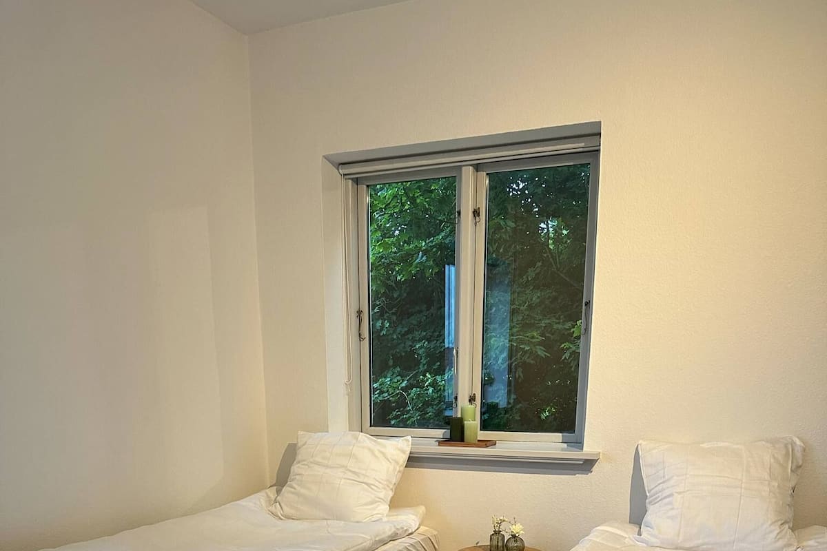 Une chambre avec deux lits simples, une petite table ronde et une fenêtre donnant sur des arbres.
