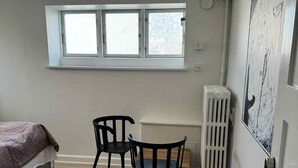 A bedroom with a bed, two chairs, a radiator, and a window. - Kolding City Rooms (Kolding)