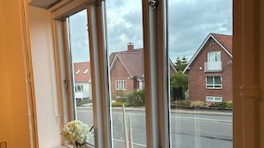 A room with a large window overlooking a street. There is a radiator under the window and a vase with flowers on the windowsill. - Kolding City Rooms (Kolding)