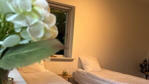 A bedroom with two single beds, a bedside table with a lamp, a window with blinds, and a plant in a vase. - Kolding City Rooms (Kolding)