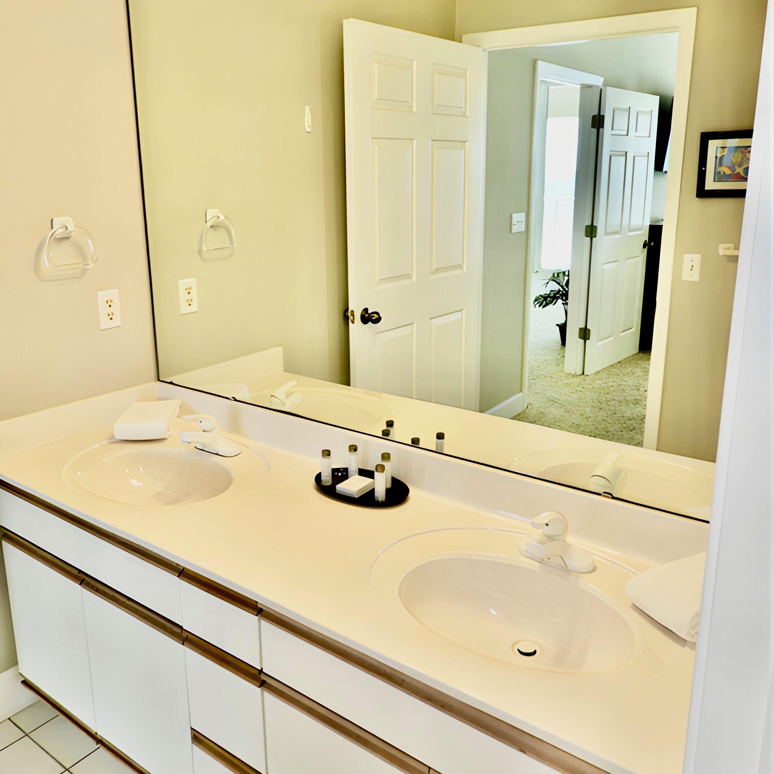 A bathroom with two sinks, a large mirror, and a door leading to another room.