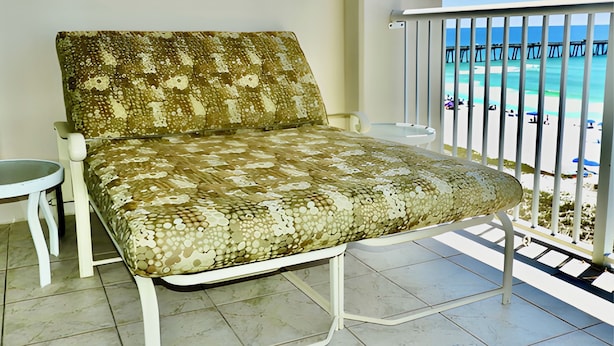 Un balcon avec un fauteuil confortable, une petite table et une vue sur la plage et la jetée.