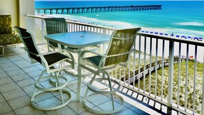 Un balcon avec une table et des chaises donnant sur une plage et une jetée.