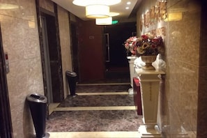 Een hotellobby met een marmeren vloer, een prullenbak, een receptiebalie en een bloemenarrangement.