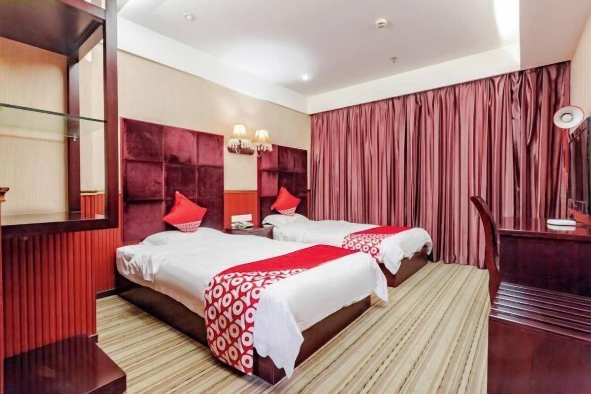 Een hotelkamer met twee bedden, een grote spiegel, een kaptafel met spiegel en een rood gordijn.